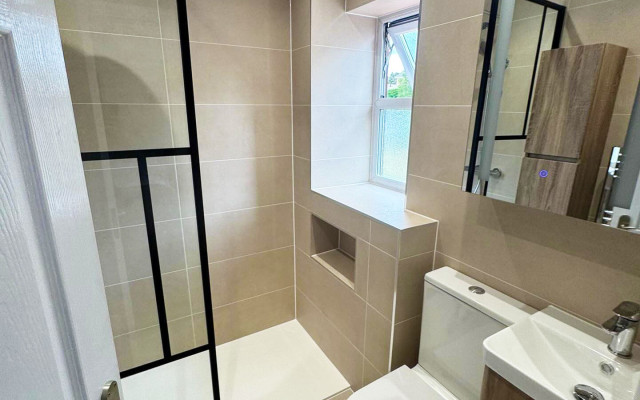 A clean bathroom featuring a shower, toilet, and basin, with neutral-colored tiles and bright lighting
