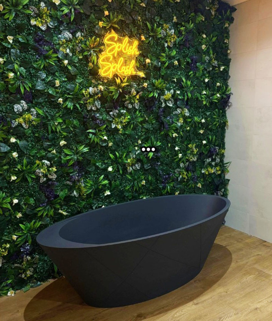 A modern bathroom featuring a green wall and a sleek black bathtub.