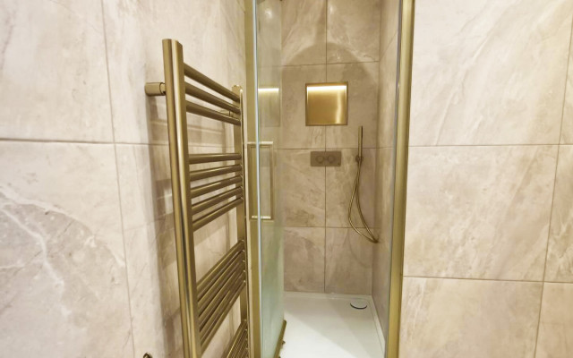 A modern bathroom featuring a shower and a stylish gold towel rack against a neutral backdrop