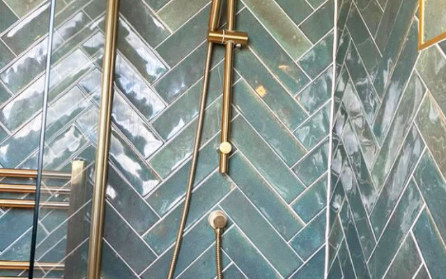 A stylish shower featuring a herringbone tile wall and an elegant gold shower head.